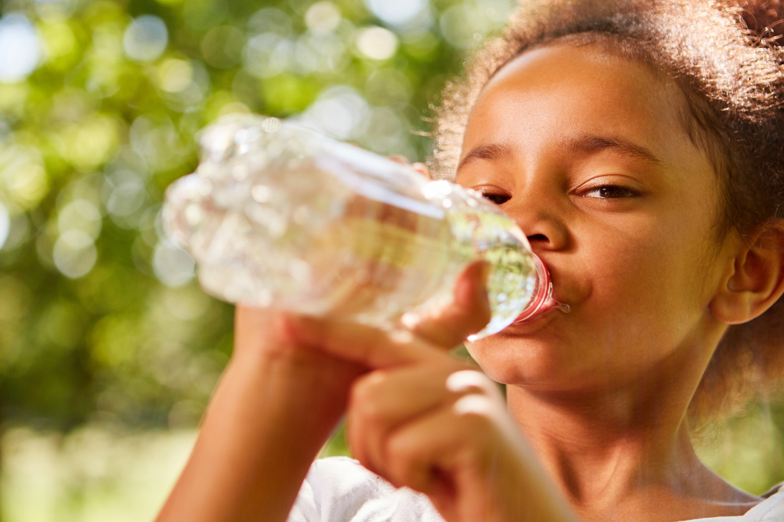 Young girl drinking water from a bottle in sunny weather, emphasizing hydration and electrolytes for active kids