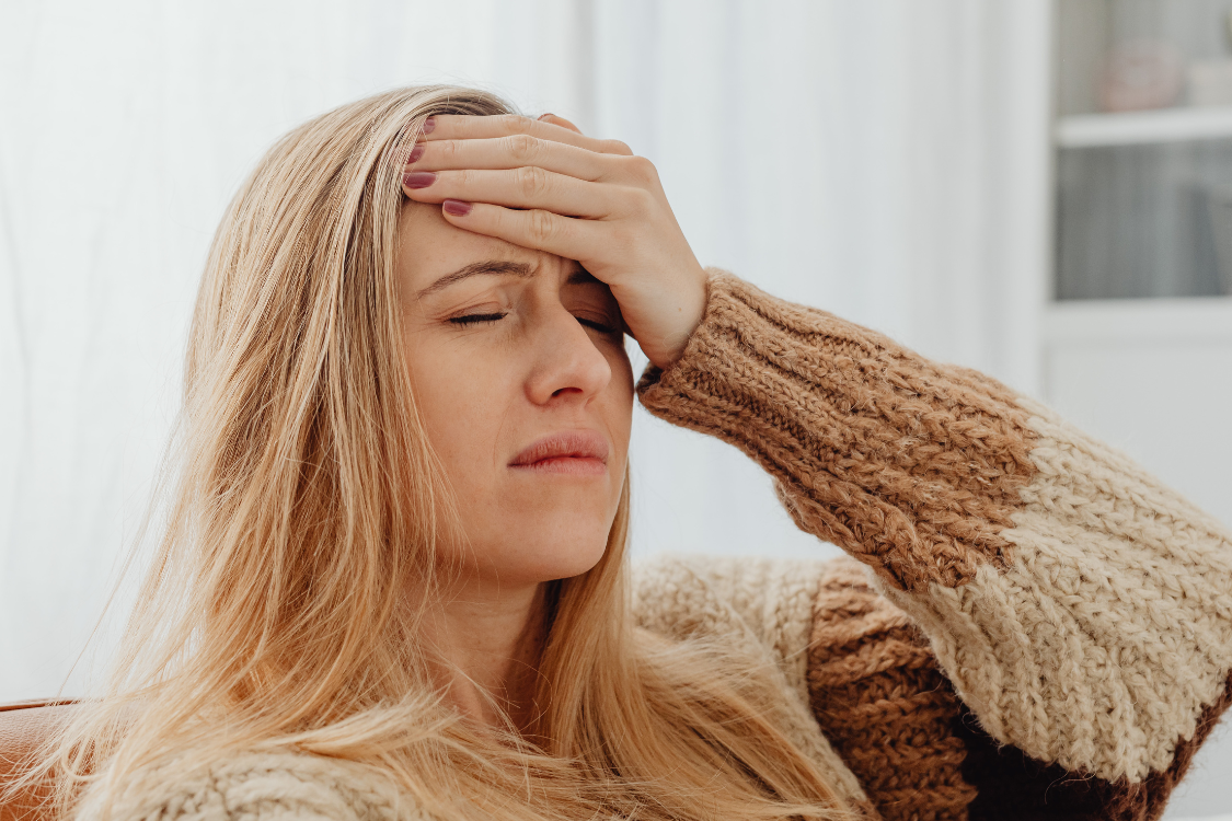 Close-up of a woman holding her forehead, representing the headache and fatigue that can fatigue be caused by dehydration.