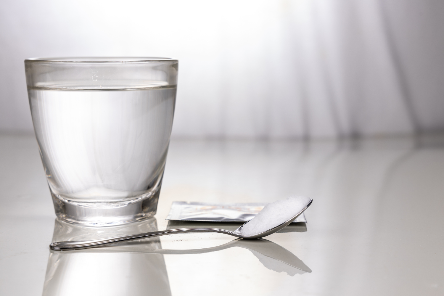 Glass of water with spoon of electrolyte powder beside it