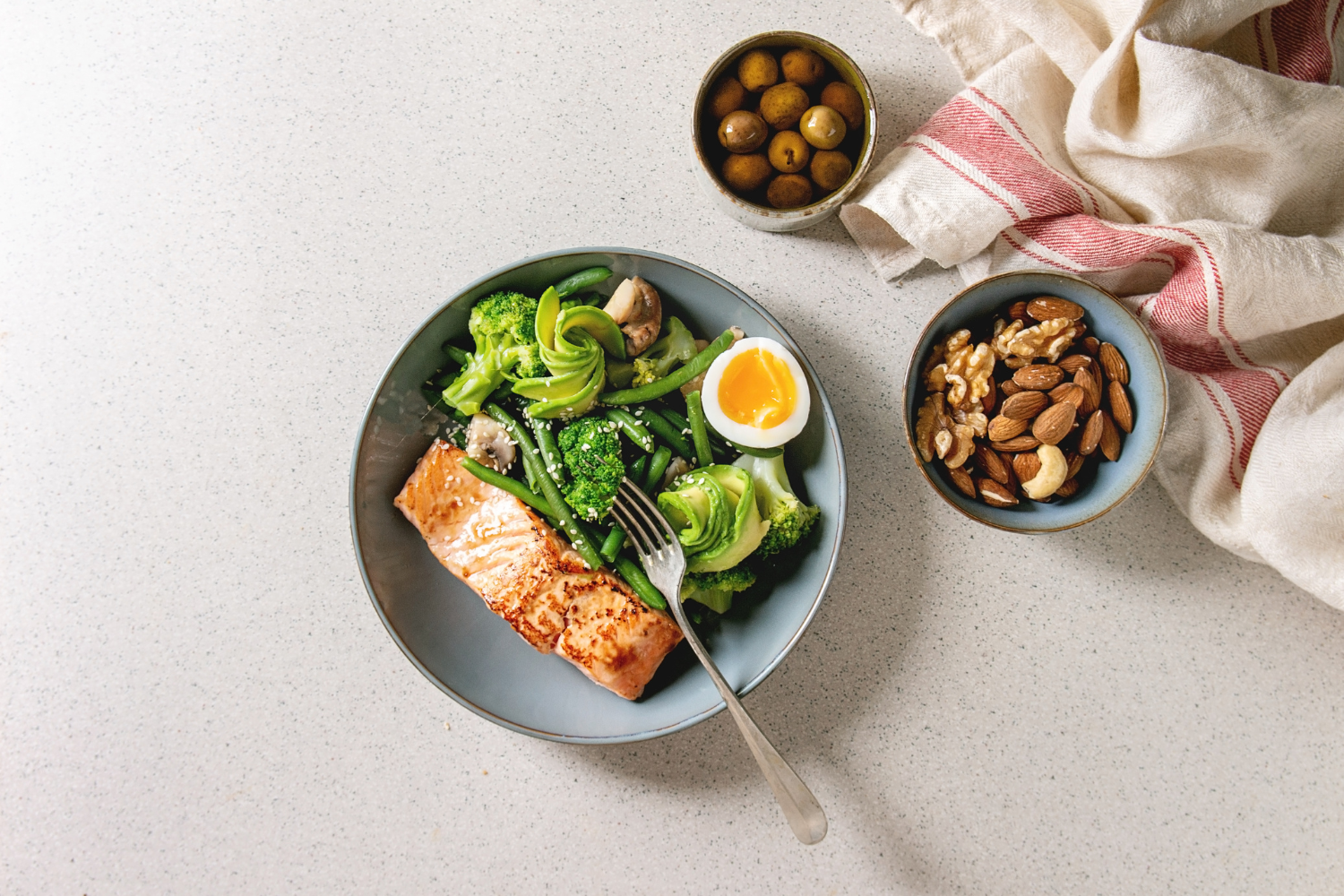 Plate of ketogenic food with nuts, avocados, fish, and leafy greens.