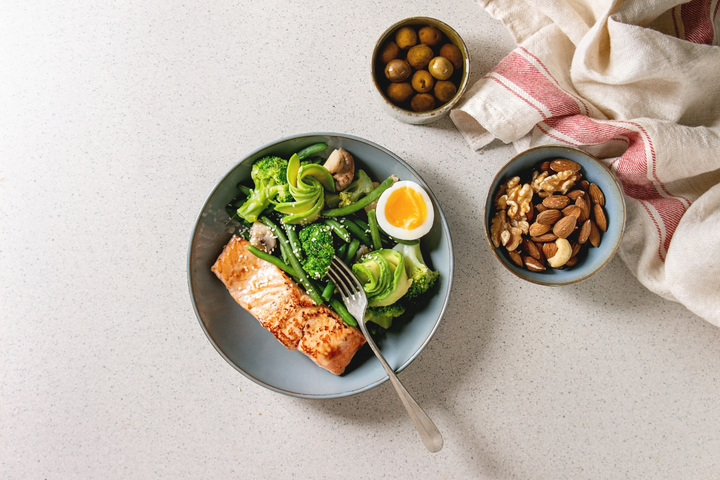 Plate of ketogenic food with nuts, avocados, fish, and leafy greens.