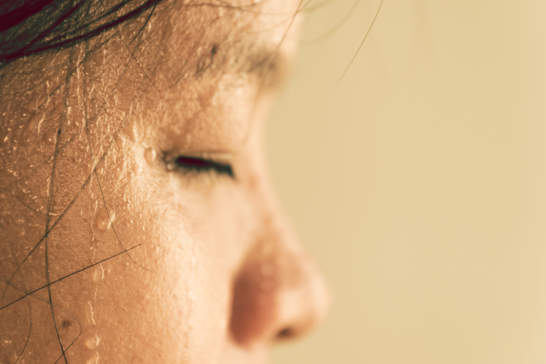 Close-up of a sweaty face during heat, a time when signs you need electrolytes can appear.