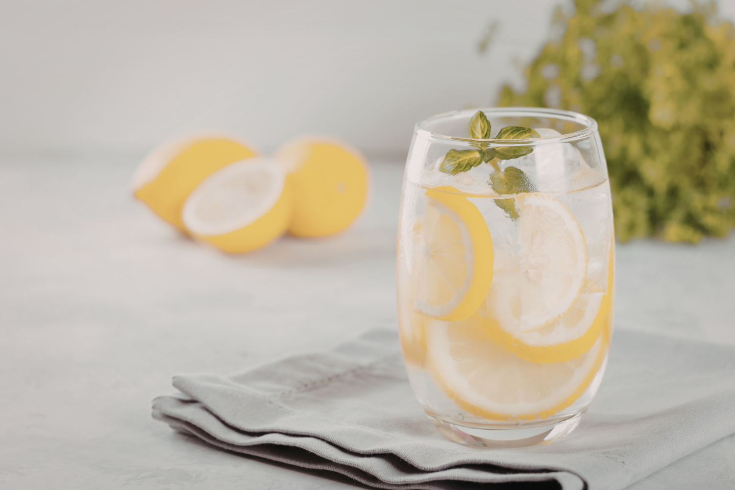 Hand adding liquid electrolyte drops to a glass of lemon water, illustrating combined hydration methods.