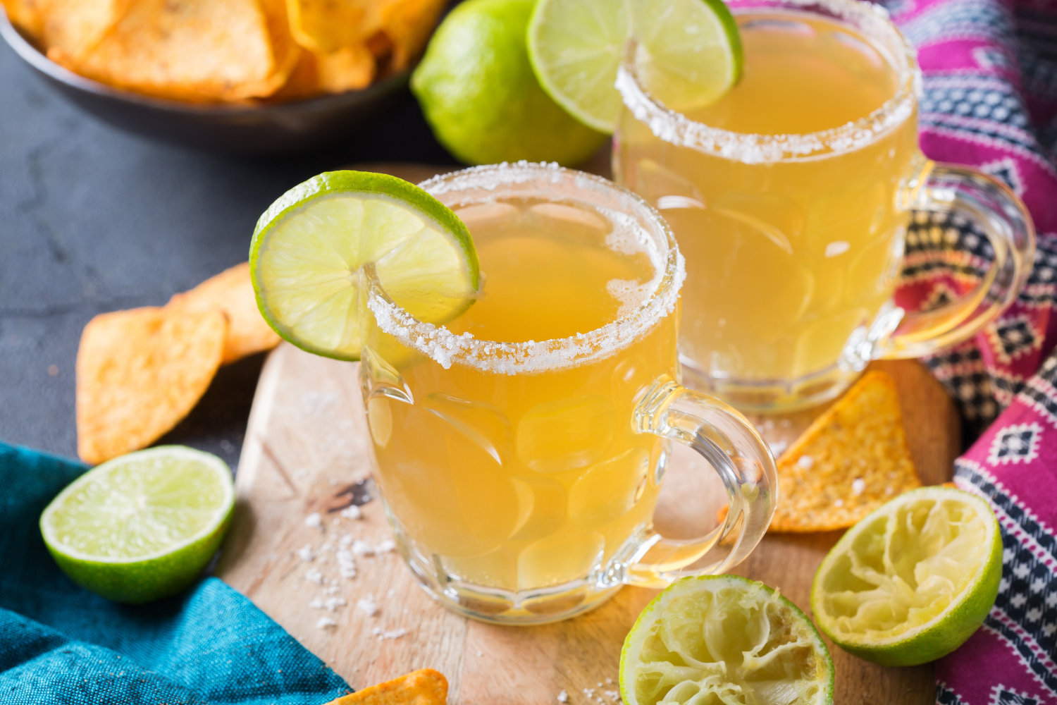 Two electrolyte-infused citrus mocktails with salted rims and lime garnishes next to party snacks.