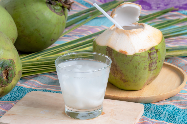 A fresh green coconut with a hole cut into it sitting next to a clear glass filled with coconut water, a natural source of potassium and other minerals.