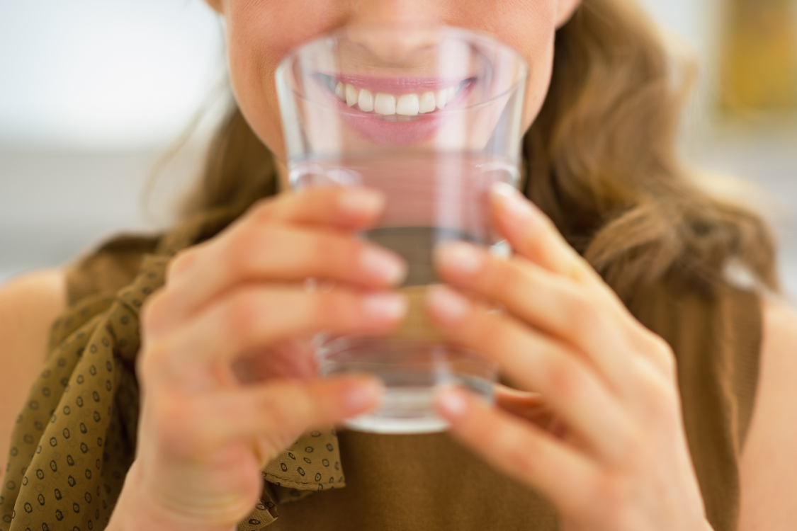Close-up of a smiling woman holding a glass of water, symbolizing hydration and morning routine electrolytes.