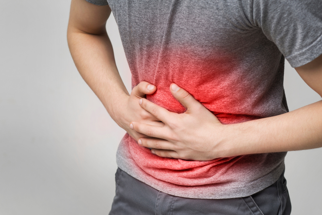 A person clutching their painful stomach with a red overlay, depicting the discomfort and vomiting symptoms of stomach flu that require electrolyte drinks.